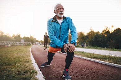 Senior bearded man jogging on a running track outdoors, in a tracksuit.